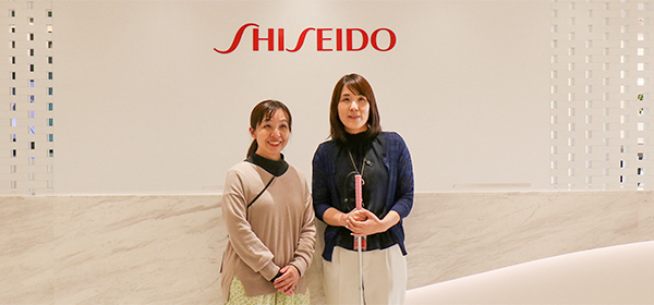 写真：赤と白を基調とした資生堂ジャパン本社エントランスでの写真。左が菅谷さん、右が石川さん