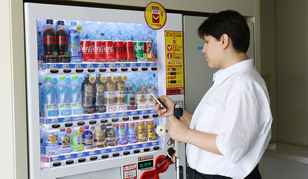 写真：視覚障がい者がコカ･コーラの自販機でスマートフォンを操作している所